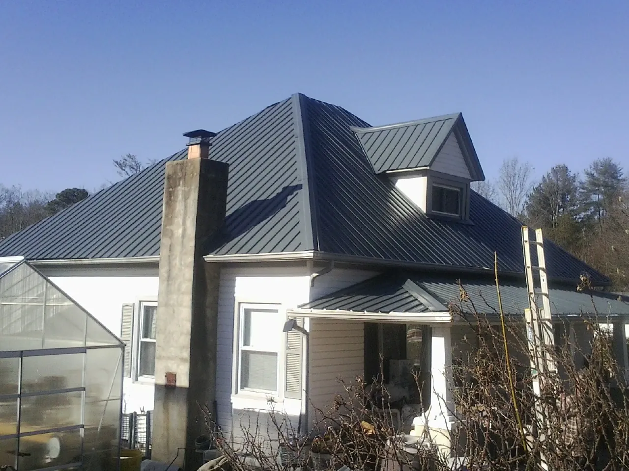 Dark blue standing seam metal roof on a white farmhouse with dormer — Slate & Tile Roof Repair by Roofing Brothers in Sebago