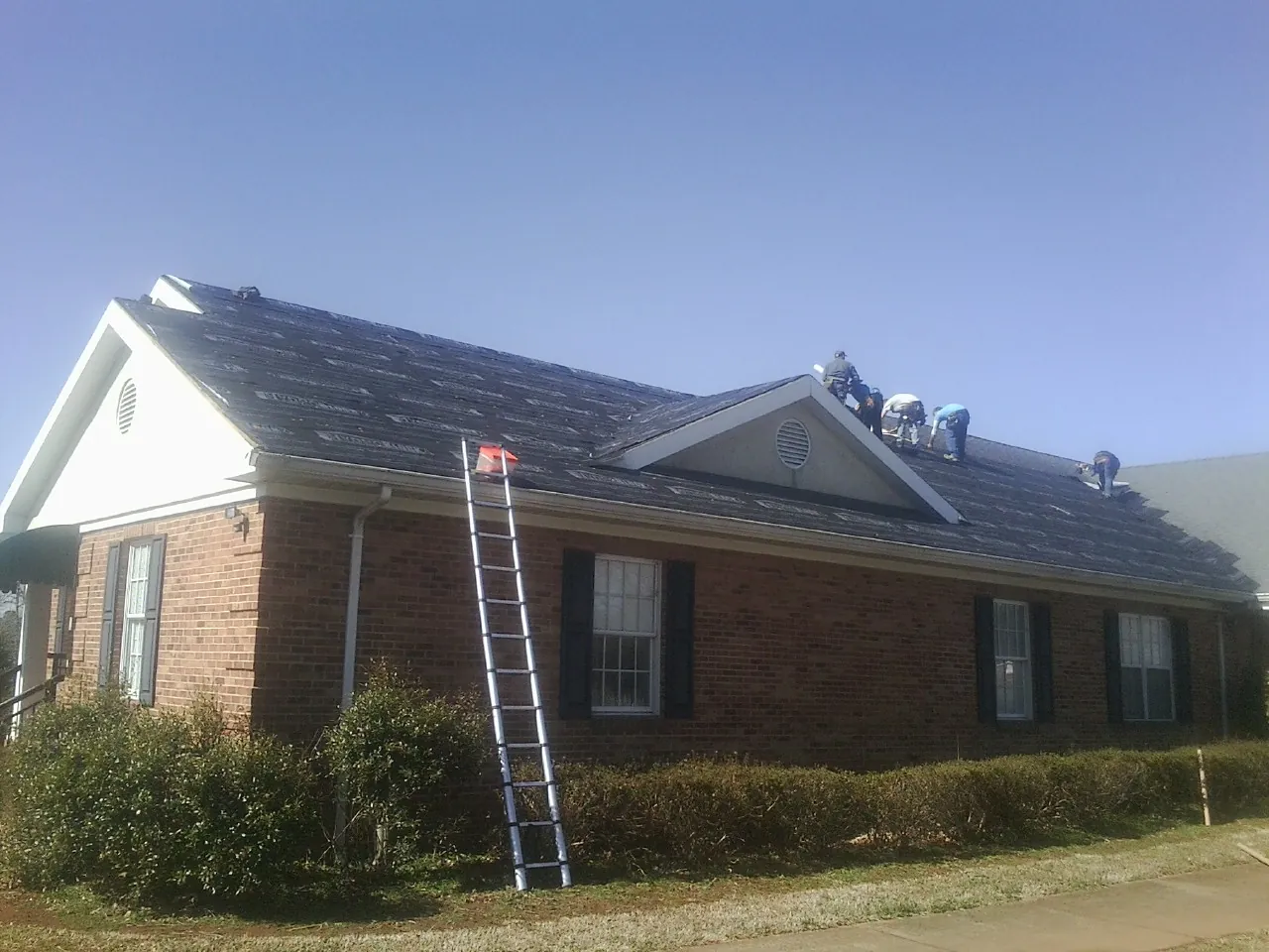 Crew tearing shingles off a brick ranch roof with a ladder set — Metal Roof Repair work by our crew in Sebago