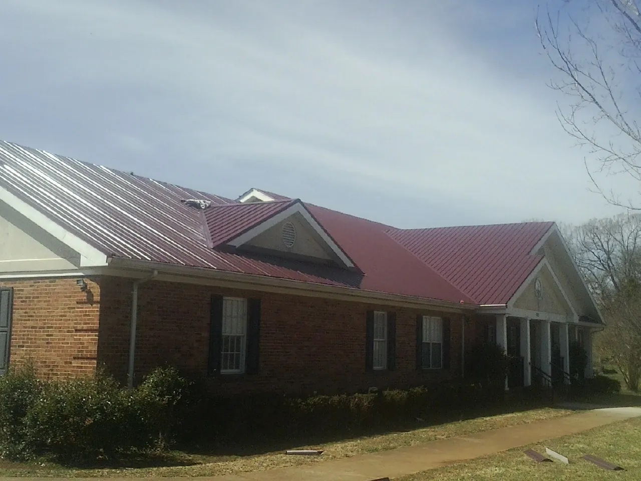 Red metal roof with gabled entries on a long brick building, from a Hail Damage Roof Repair job in Sebago
