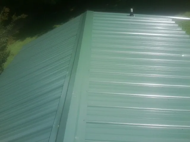 New green metal panels meeting at the ridge of a roof — Flat Roof Repair work by our crew in Sebago