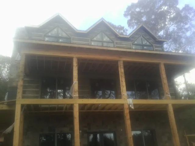 Dormers and porch framing on a large log home under construction — Roof Coating work by our crew in Sebago