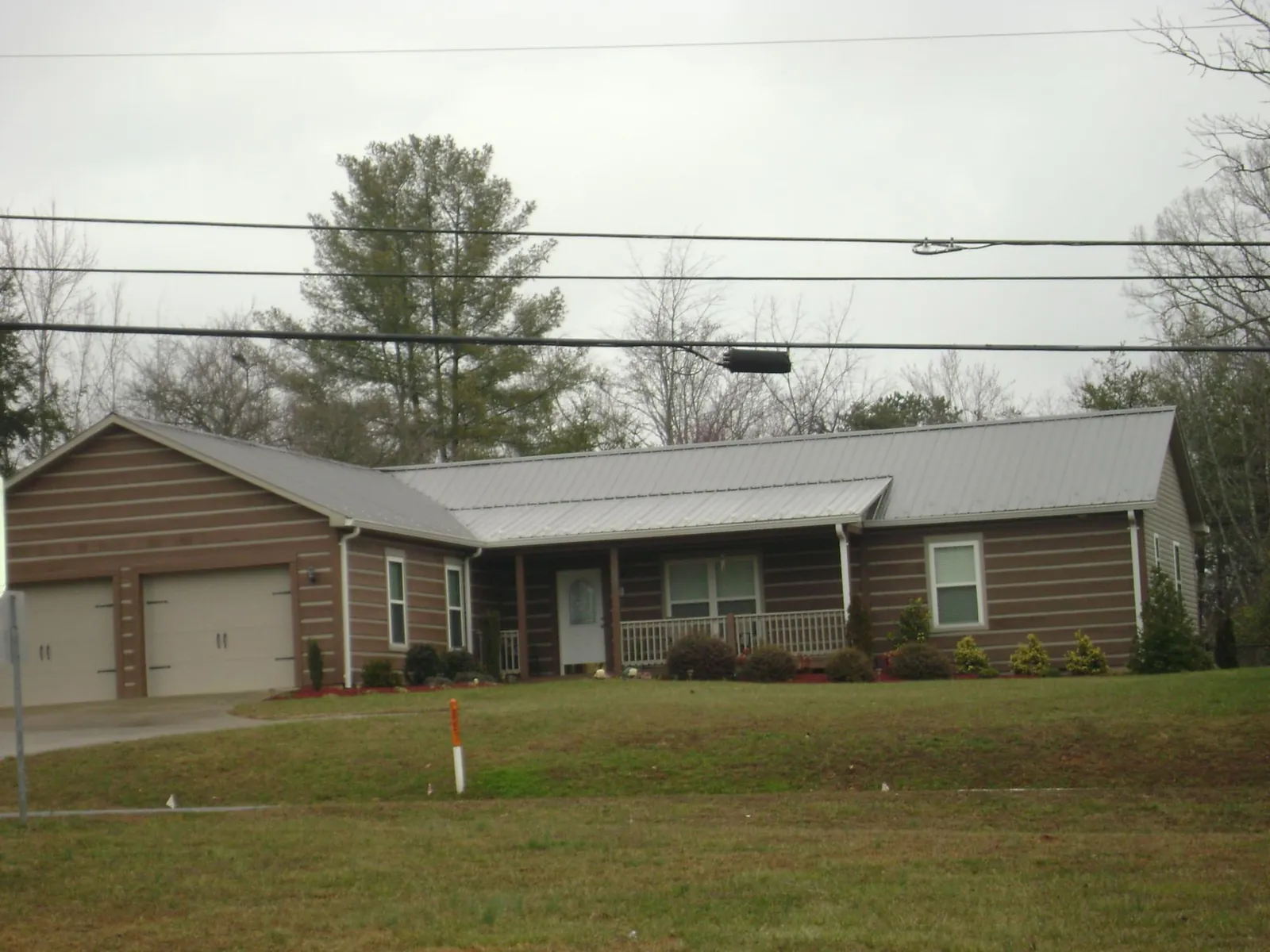 Gray metal roof on a log sided ranch home with a front porch in Sebago