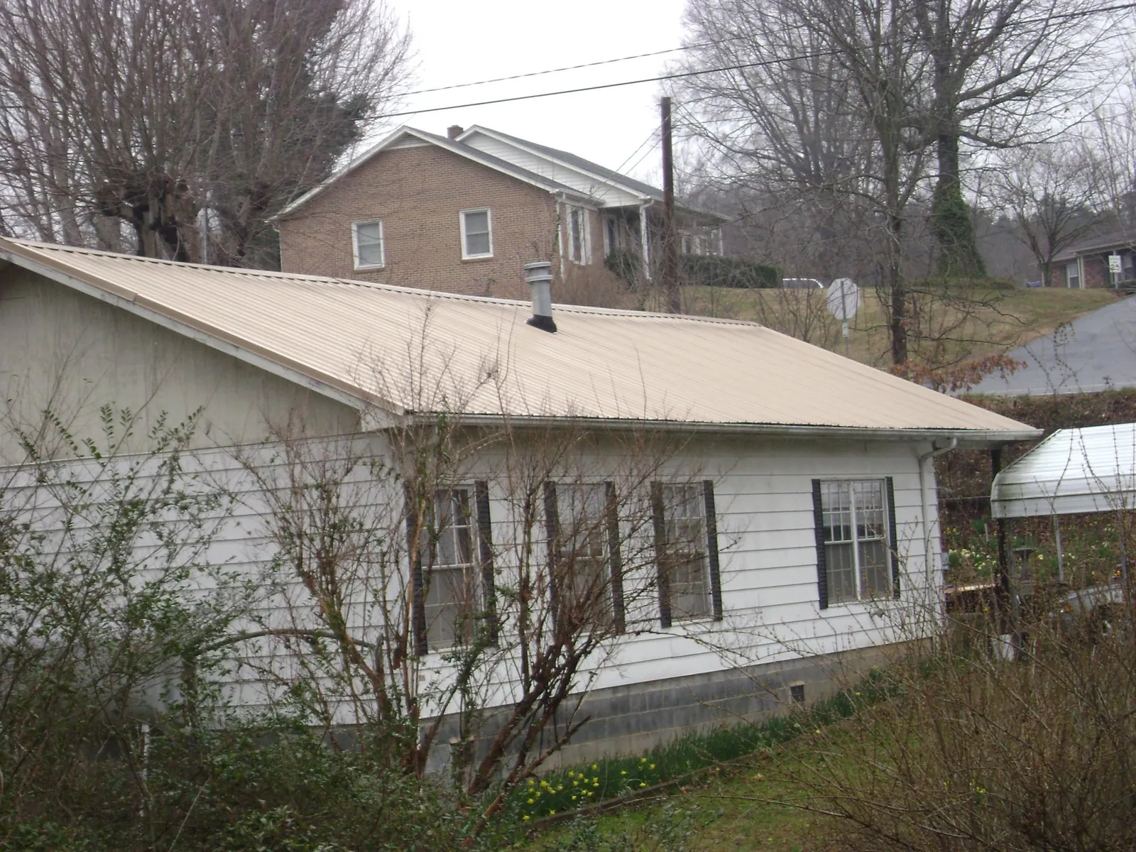 Tan metal roof on a white sided house set into a hillside — Commercial Roofing by Roofing Brothers in Sebago
