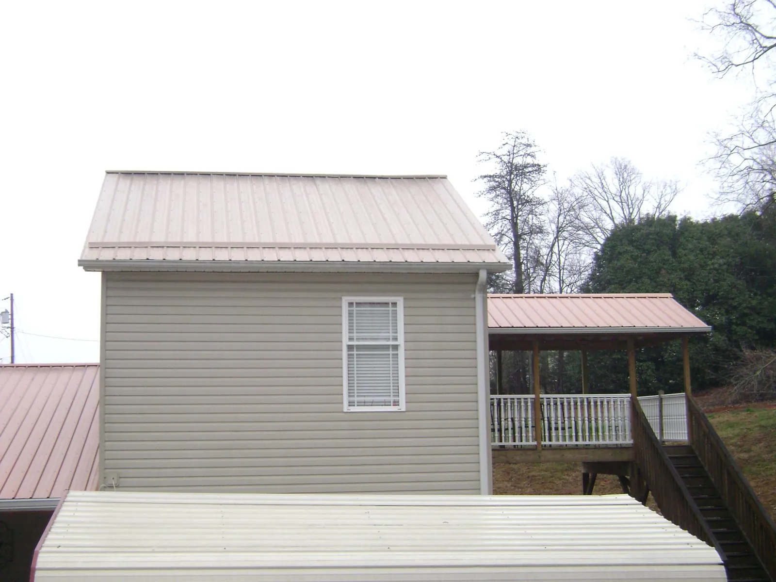 Tan metal roofs on a two story addition and attached porch, from a Roof Replacement job in Sebago